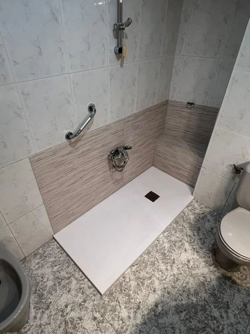 Baño después de la reforma: plato de ducha blanco con alicatado a media altura y barra de apoyo