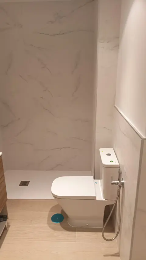 Baño con paredes de efecto mármol, suelo de imitación madera y plato de ducha blanco