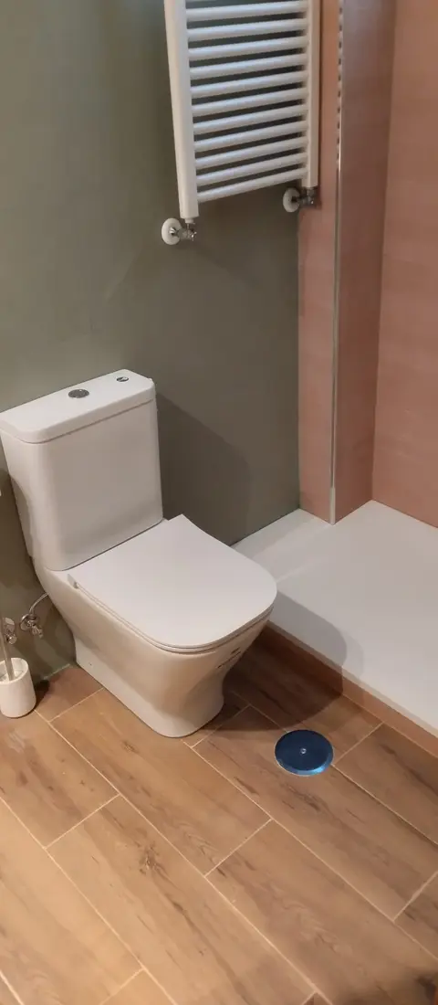 Baño con suelo de imitación madera, plato de ducha blanco y toallero