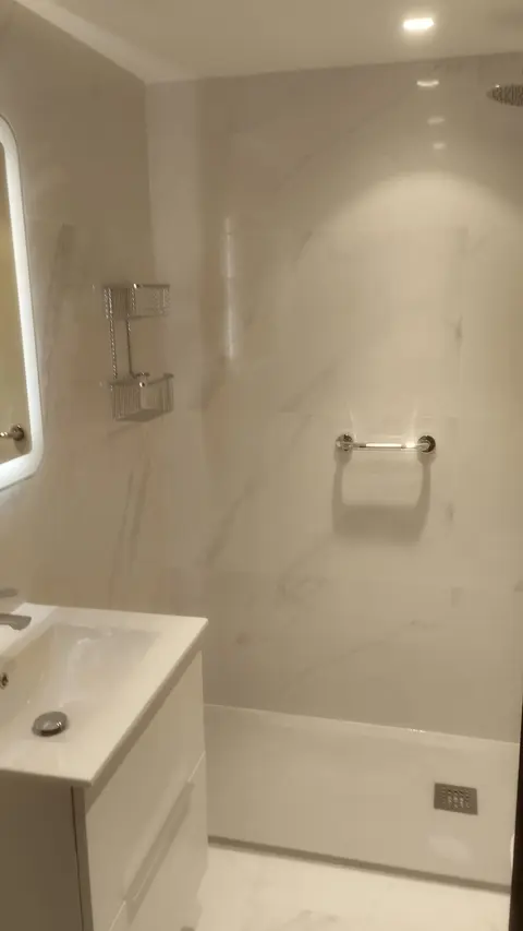Ducha con revestimiento de efecto mármol, plato blanco y lavabo suspendido