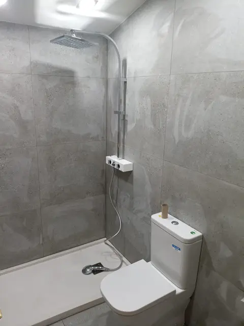 Ducha con revestimiento gris de gran formato, plato blanco y columna de lluvia