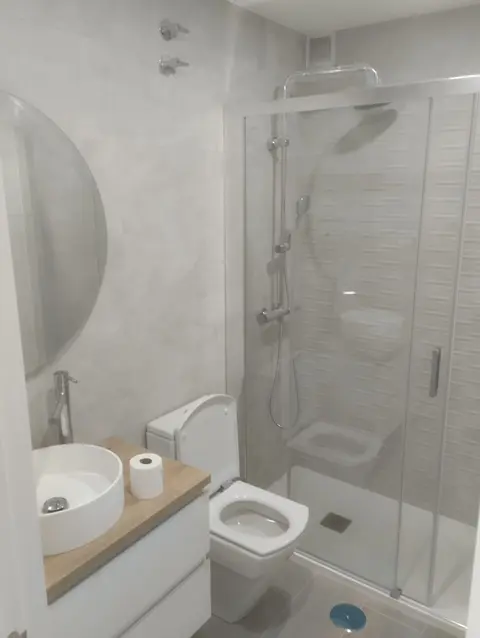 Lavabo sobre encimera de madera junto a una ducha con mampara corredera de vidrio